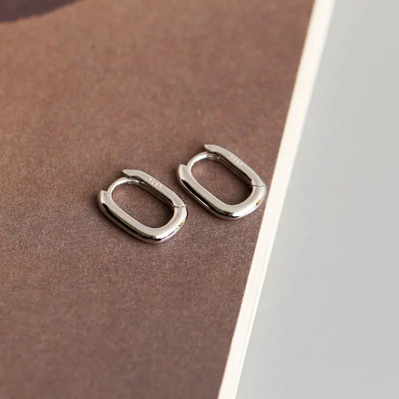 Pair of small oval-shaped 925 sterling silver earrings with polished finish and hinged ear buckle design