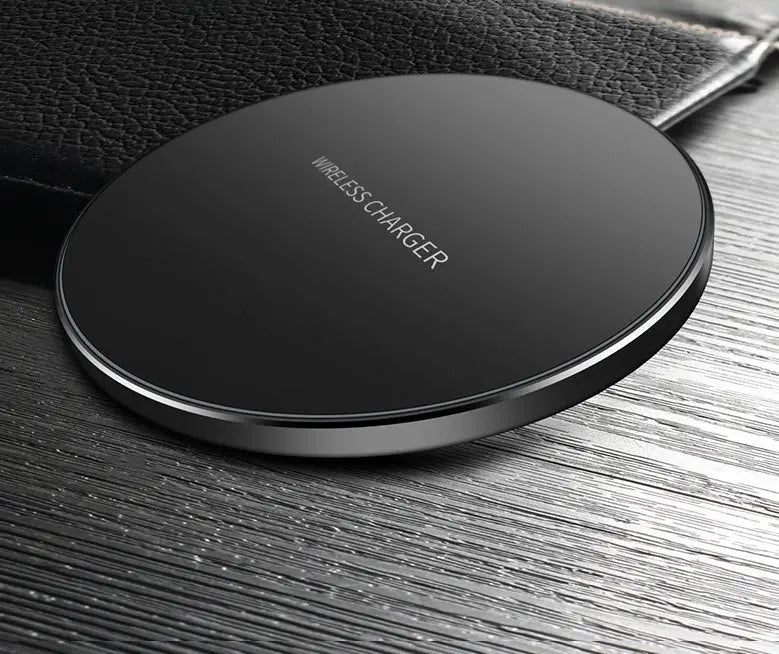 Black circular wireless charger pad with sleek design placed on textured wooden surface next to a black leather item