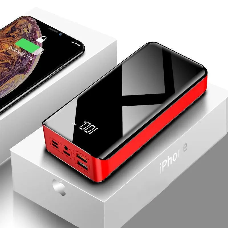 Glossy black and red 30000mAh power bank with digital display showing 100% charge, placed on an iPhone box next to a charging smartphone