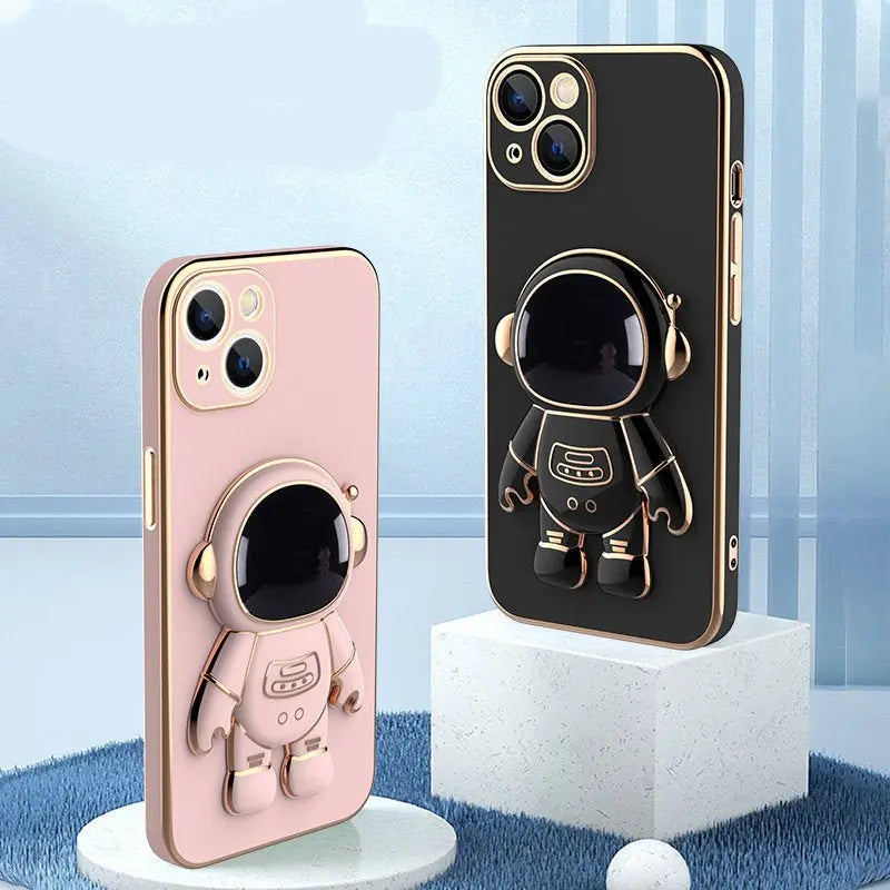 Two iPhone cases with 3D astronaut design, one in pink and one in black with gold trim, standing on display platforms