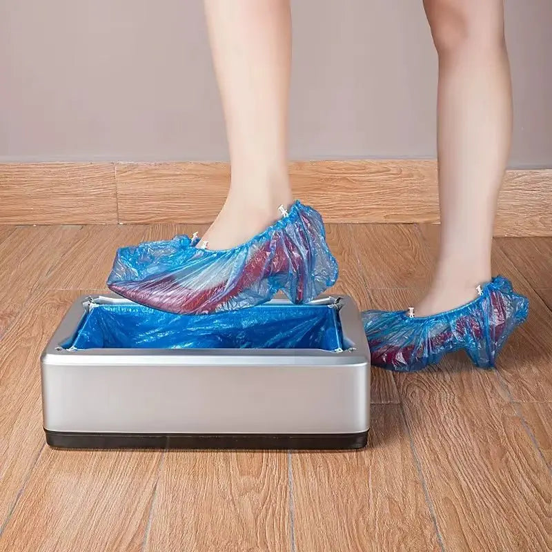 Silver automatic hand-free shoe cover dispenser with feet wearing blue plastic shoe covers on wooden floor