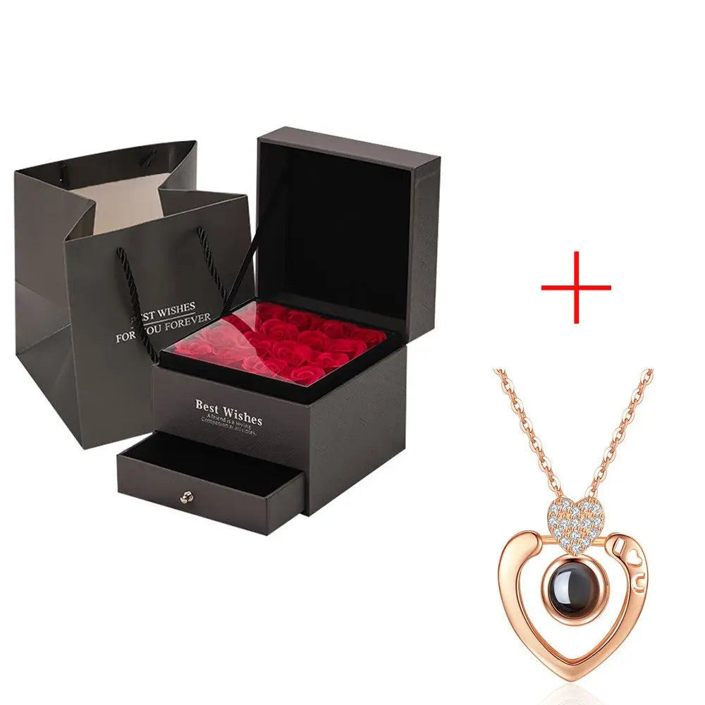 Black gift box with preserved red roses and drawer alongside rose gold heart pendant necklace with black center stone