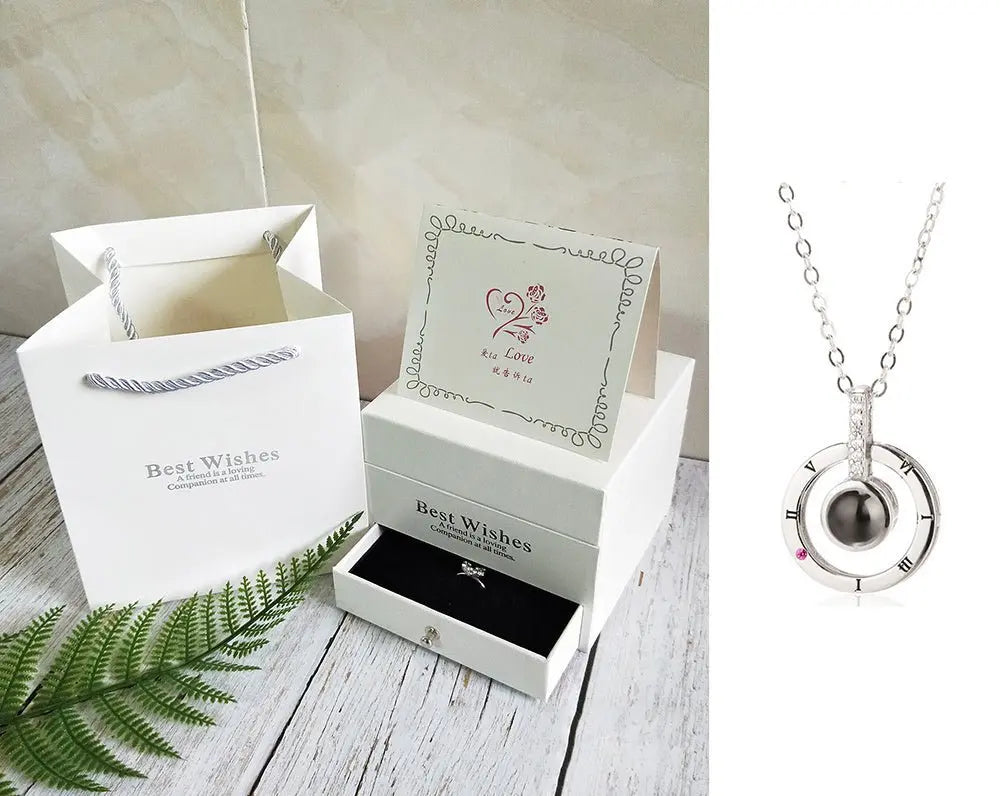 White gift box with a silver pendant necklace, greeting card, and matching white gift bag on wooden surface