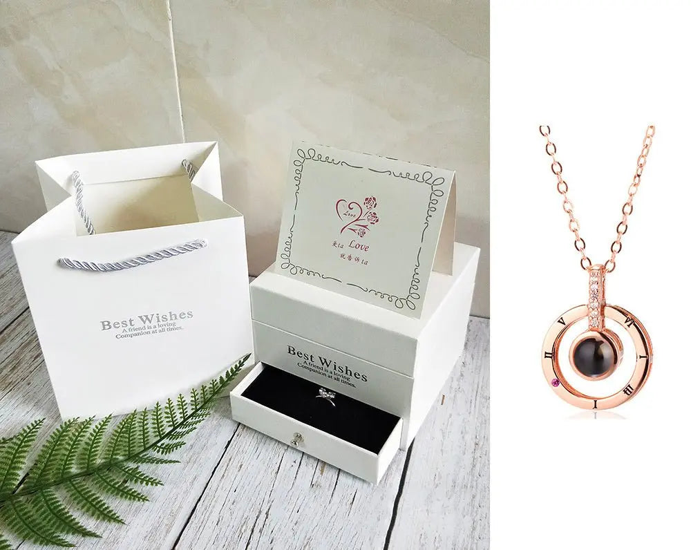 Rose gold circular pendant necklace with black stone displayed next to white gift box set with card and gift bag