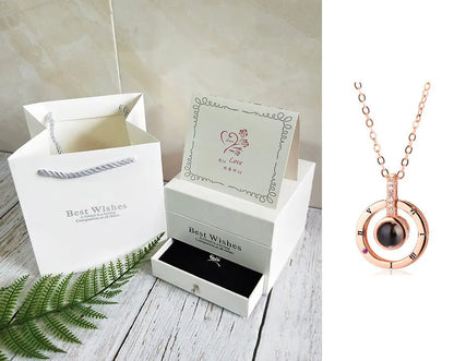 Rose gold circular pendant necklace with black stone displayed next to white gift box set with card and gift bag