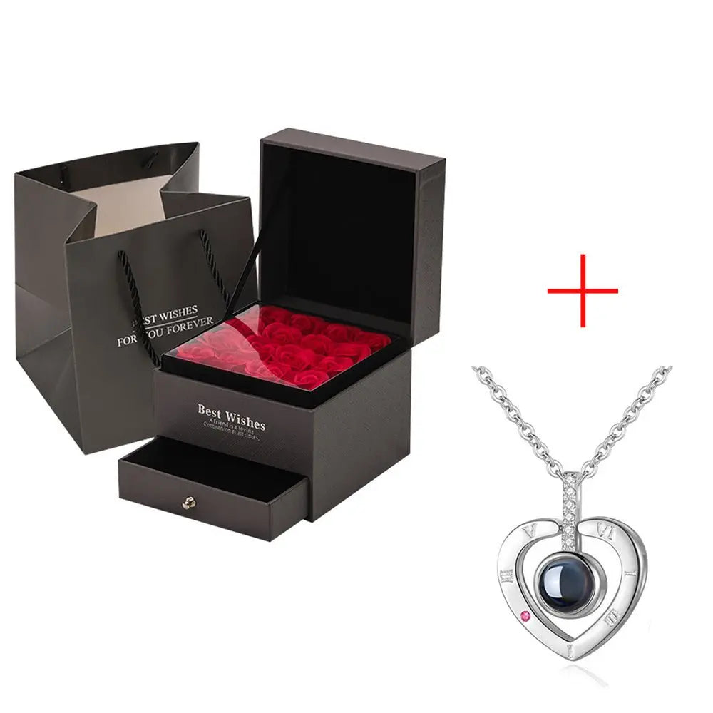 Black gift box with preserved red roses and silver heart-shaped pendant necklace on white background