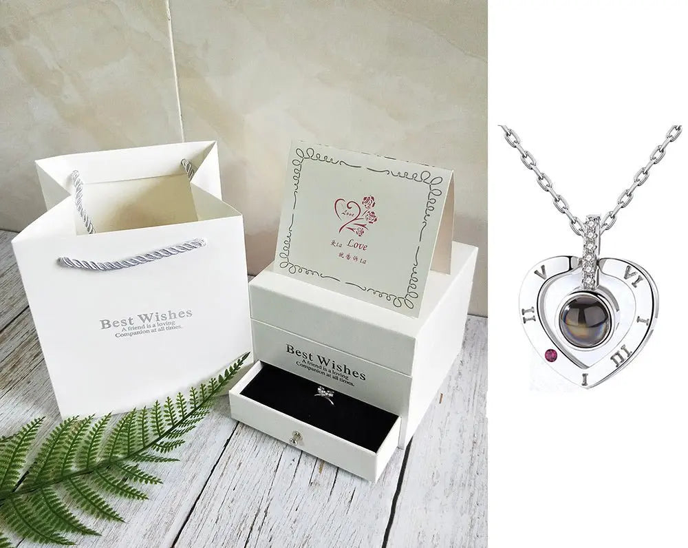 White gift box and bag set with greeting card and silver heart-shaped rose necklace featuring Roman numerals and gemstone detail
