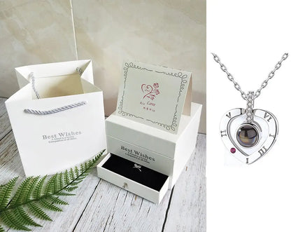 White gift box and bag set with greeting card and silver heart-shaped rose necklace featuring Roman numerals and gemstone detail