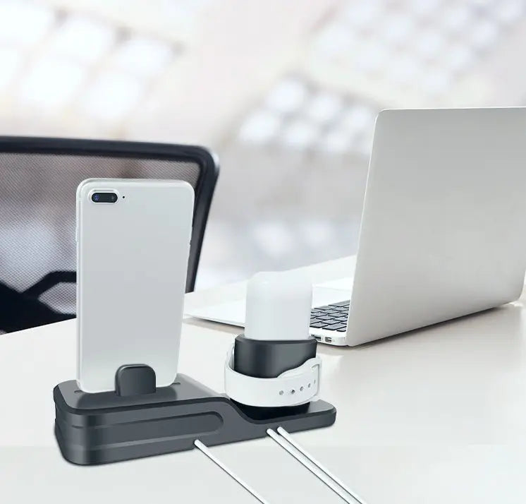 Black 3-in-1 charging base holding a white smartwatch, white earbuds case, and white smartphone on office desk