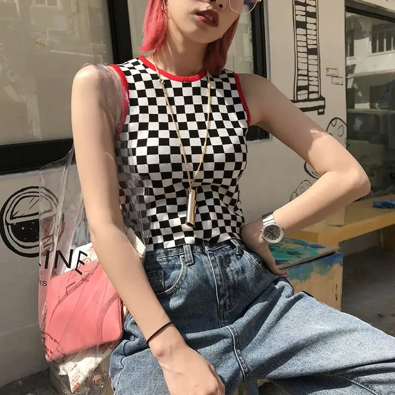 Woman wearing sleeveless black and white checkered crop top with red trim paired with high waist blue jeans and accessories