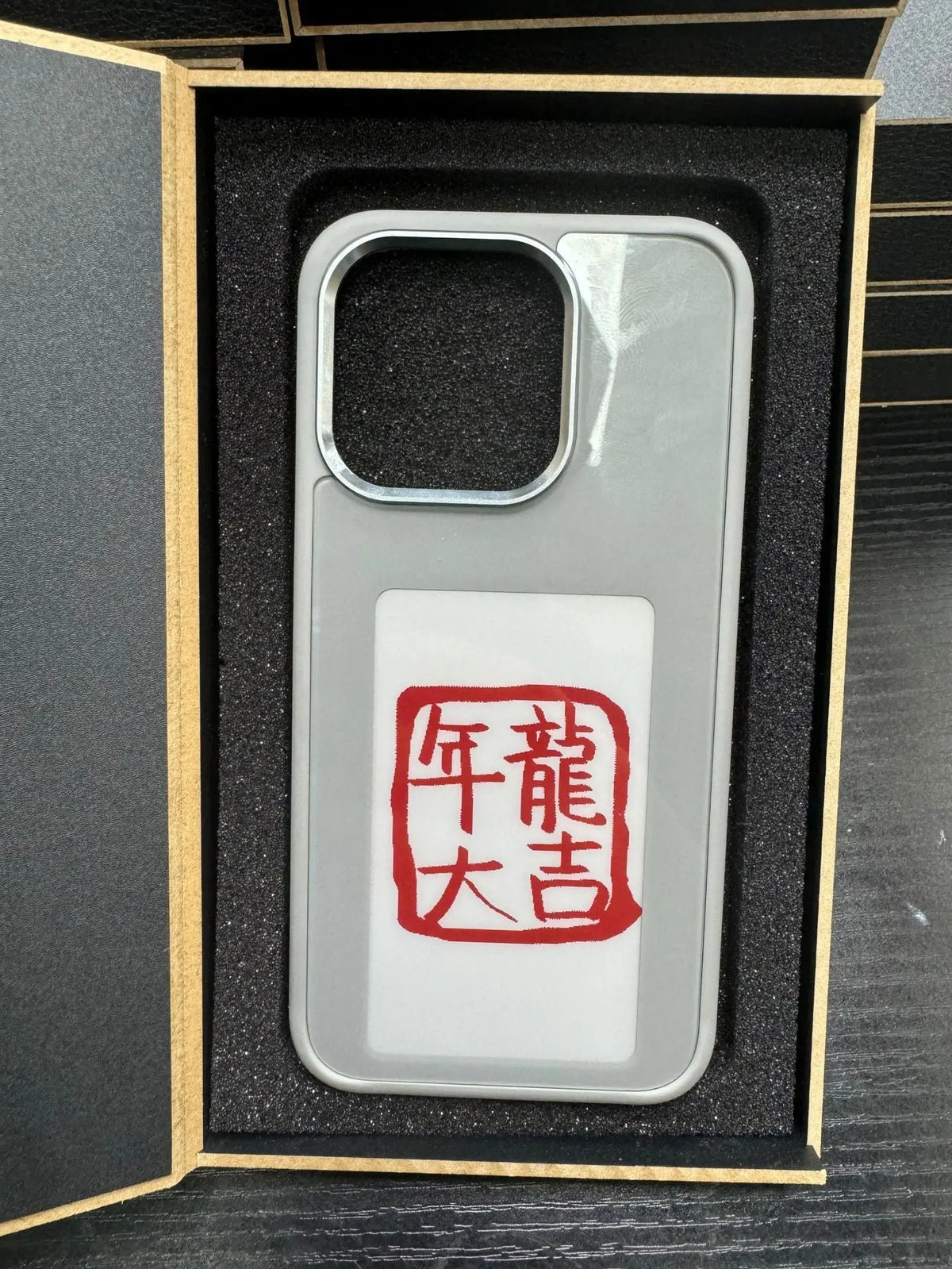 Silver E-ink screen phone case with red Chinese calligraphy design, displayed in protective black foam packaging