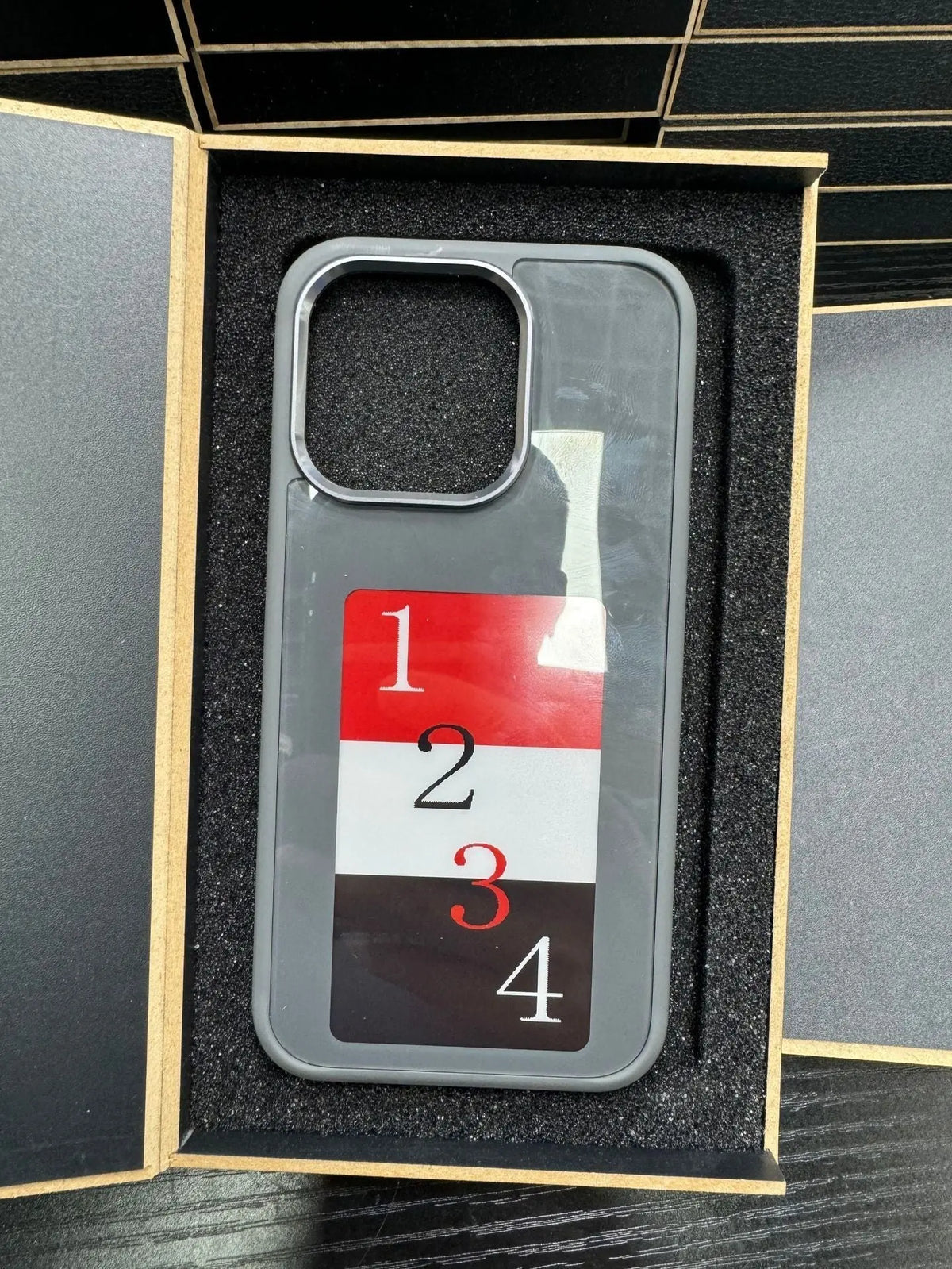 Gray E-ink phone case with numbered design in black foam-lined luxury packaging box opened flat