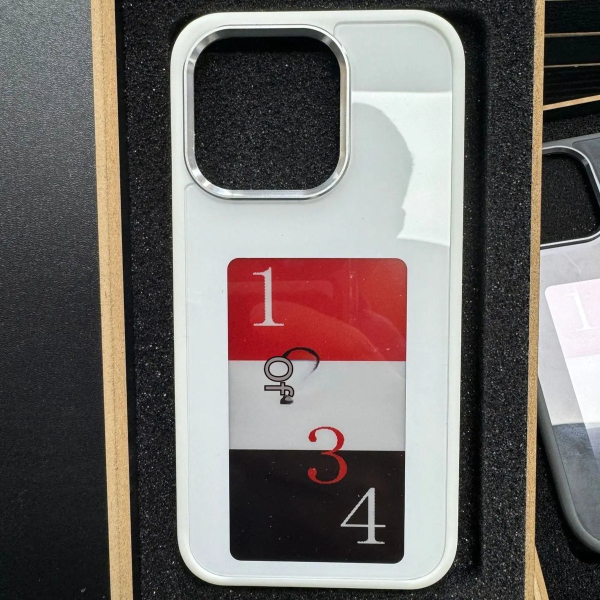 White E-ink screen phone case with black, red, and white segmented personalized design in protective foam tray