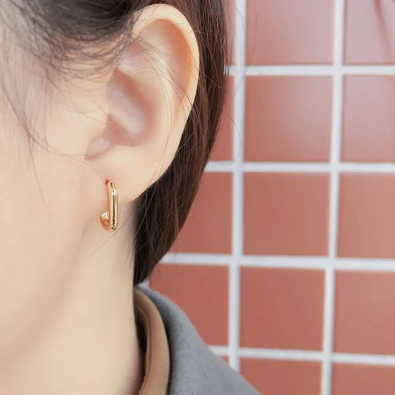 Close-up of Korean style gold-plated 925 sterling silver geometric oval loop earrings worn on ear