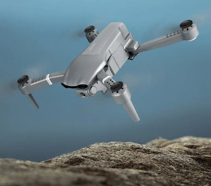 Grey folding drone in flight above rocky terrain with visible front camera and extended arms
