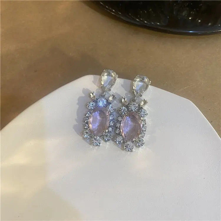 Pair of Hot Girl H Lala Diamond personalized earrings with oval pink and clear gemstone accents on white surface