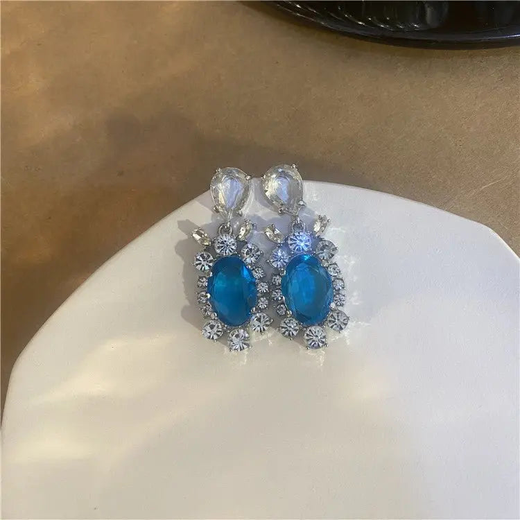 Pair of silver geometric earrings featuring large blue oval and clear teardrop crystals with surrounding small rhinestones