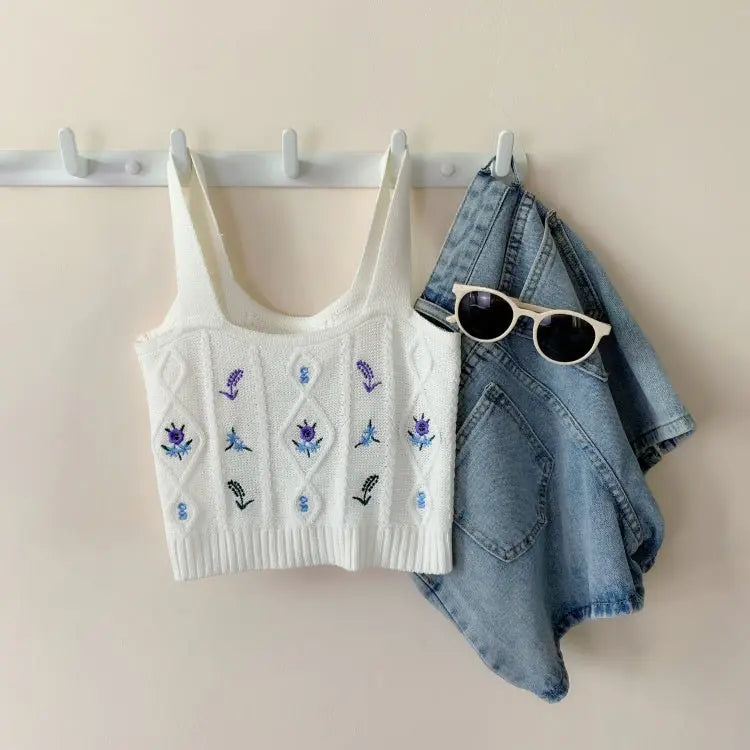 White Hyuna style crop top with purple floral embroidery hanging next to blue denim jacket and white sunglasses