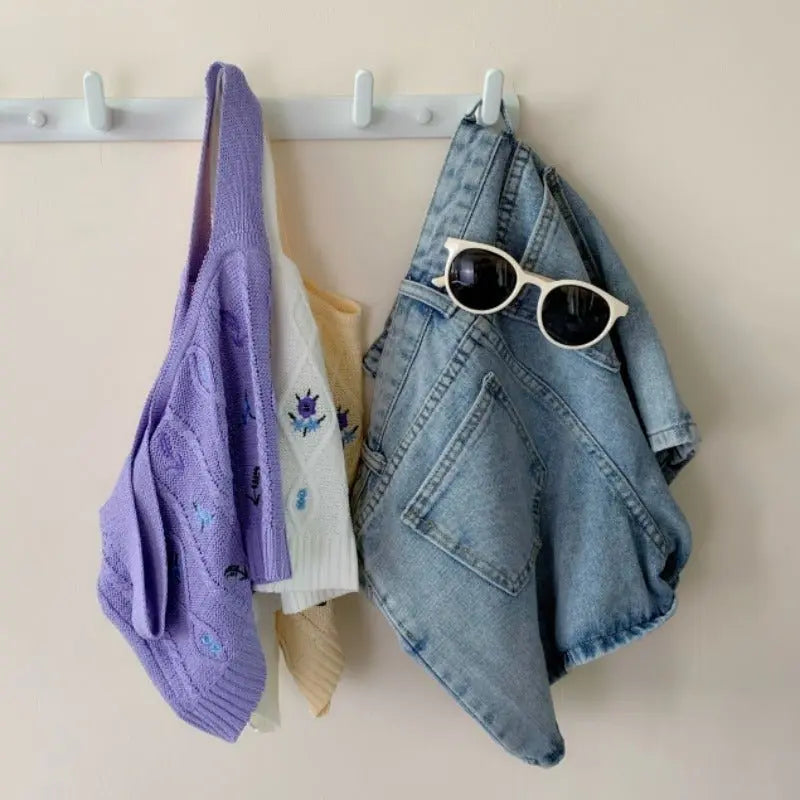 Purple Hyuna style knit crop top with embroidered flowers hanging next to white and apricot crop tops and denim shorts with sunglasses
