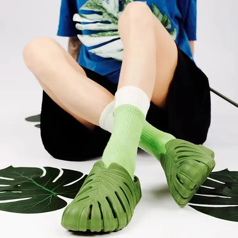 Green platform slip-on sandals with cloud sole and leaf cutout design worn with green socks on seated model