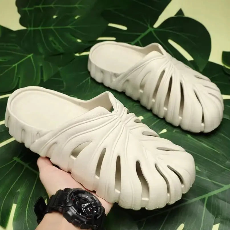 White cushioned unisex platform slip-on sandals with cutout leaf-inspired design and textured sole on green leaf background