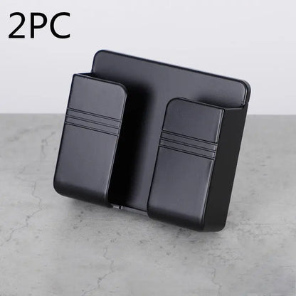 Black mobile phone charging storage rack with punch-free sticky back, shown as a 2-piece set on grey surface