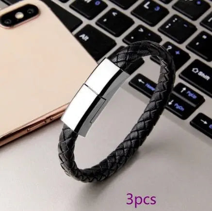 Black braided leather USB charging cable bracelet with silver magnetic clasp styled next to smartphone and laptop keyboard