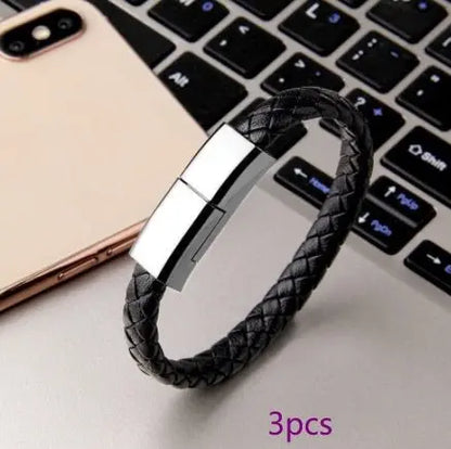 Black braided leather USB charging cable bracelet with silver magnetic clasp styled next to smartphone and laptop keyboard