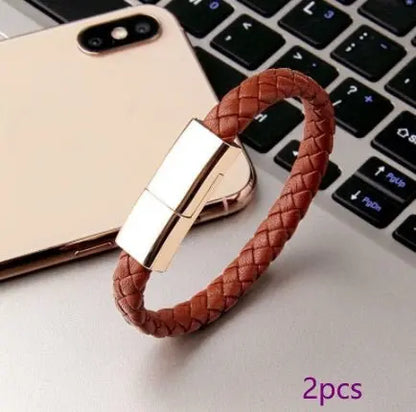 Brown braided leather bracelet charger with gold magnetic clasp for USB charging and data transfer, shown near smartphone and keyboard