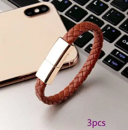 Brown braided leather USB charging cable bracelet with metallic connector placed near gold smartphone and laptop keyboard