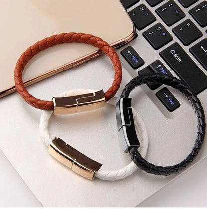 Three braided leather bracelet USB charging cables in brown, white, and black with metallic clasps on laptop keyboard