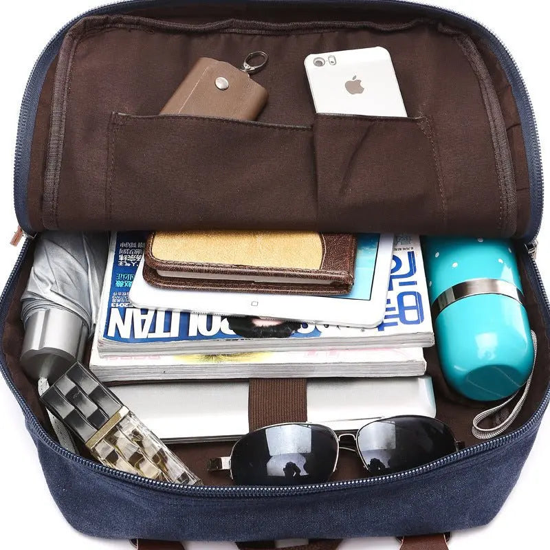 Open navy canvas backpack showing organized interior with smartphone, tablet, sunglasses, umbrella, water bottle, and magazines