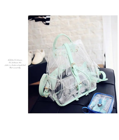 Clear backpack with mint green straps, buckles, and trim placed on black surface with small blue pouch nearby