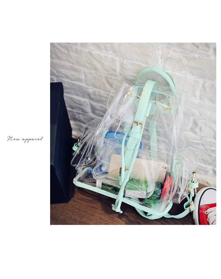 Clear backpack with mint green straps and gold buckle details placed on wooden surface against white brick wall