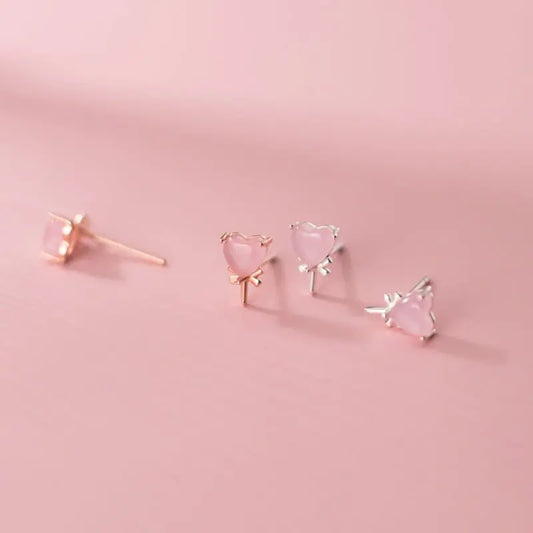 Close-up of small pink heart-shaped crystal love candy earrings in silvery and rose gold settings on pink background