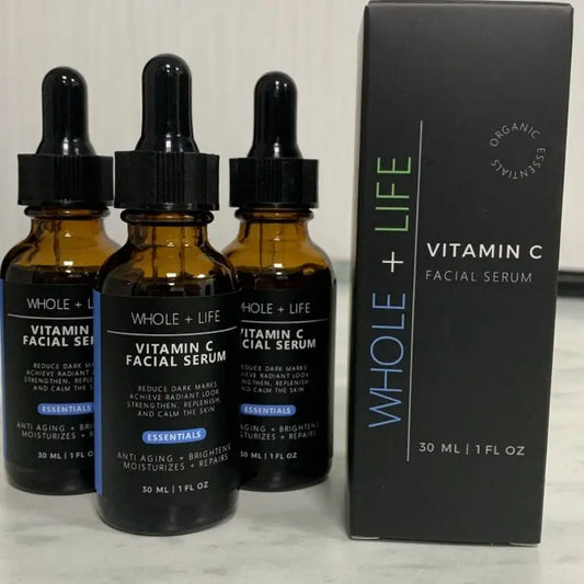 Three amber glass bottles and a black box of Whole + Life Vitamin C Facial Serum with dropper caps and product details visible