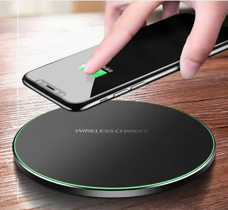 Black round wireless charger pad with green LED edge charging a smartphone held above it on wooden surface