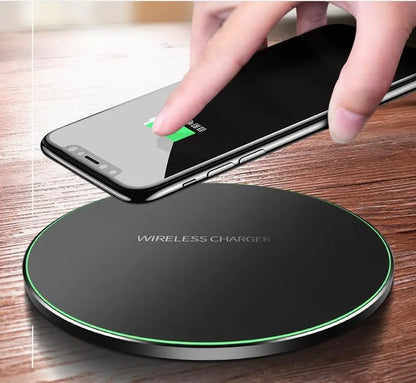 Black round wireless charger pad with green LED edge charging a smartphone held above it on wooden surface
