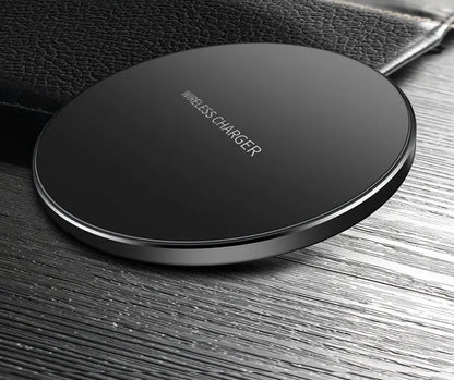 Black circular wireless charger pad with sleek design placed on textured wooden surface next to a black leather item