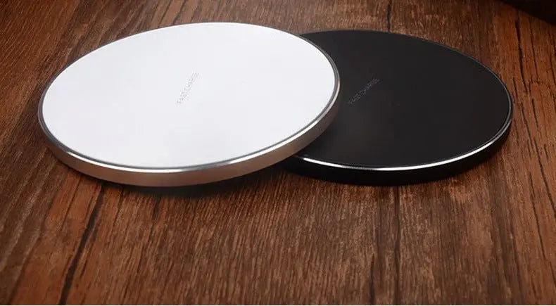 Black and white slim wireless charging pads for iPhone and Samsung with metallic edges on wooden surface
